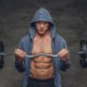 Abdominal man in a blue hoodie holds barbell.