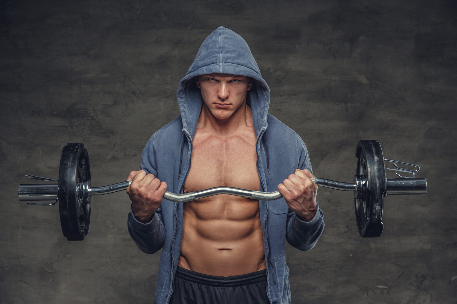 Abdominal man in a blue hoodie holds barbell.