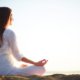Side view of meditating woman sitting in pose of lotus against clear sky outdoors